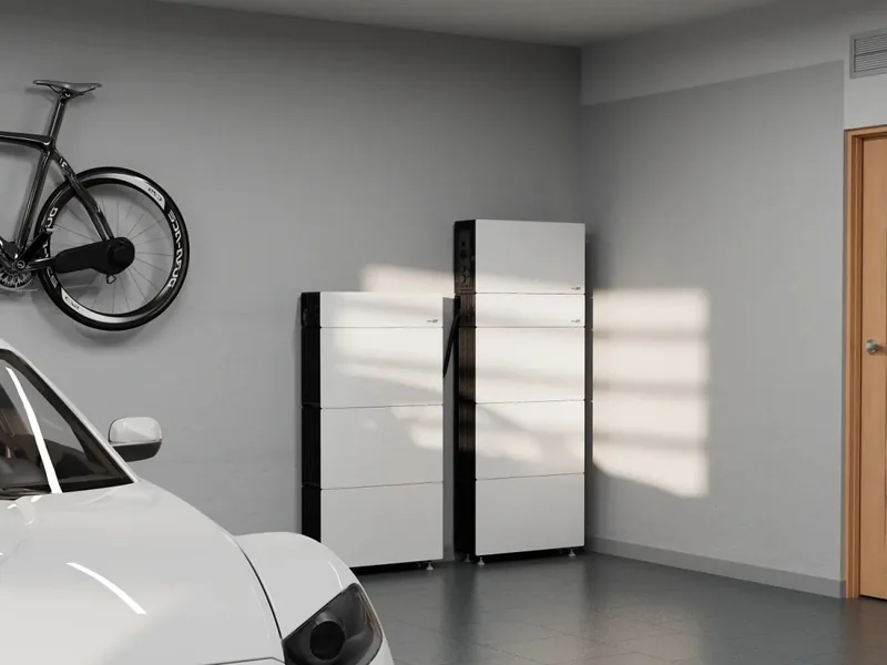 Two white SolarEdge Nexis battery stacks against a garage wall, beside a parked car and a bike on the wall